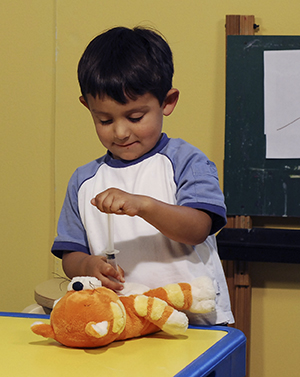 Boy playing with pretend syringe and teddy bear.